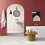 Freestanding bathtub and rattan table in the bathroom with brick-red wall and marble tiles, view of the sink through the arched